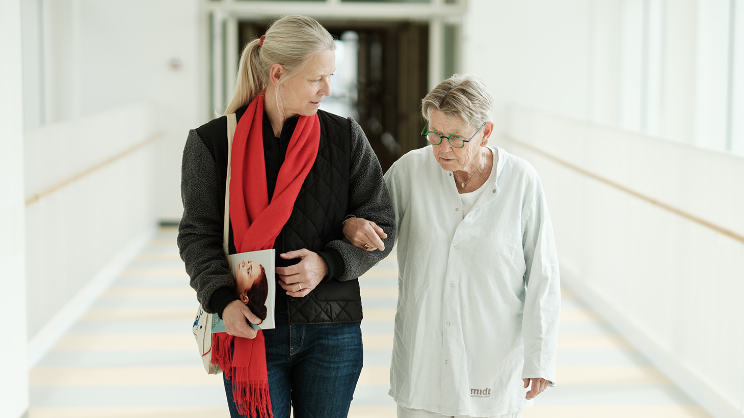 Patient og pårørende går arm i arm på hospitalsgang.