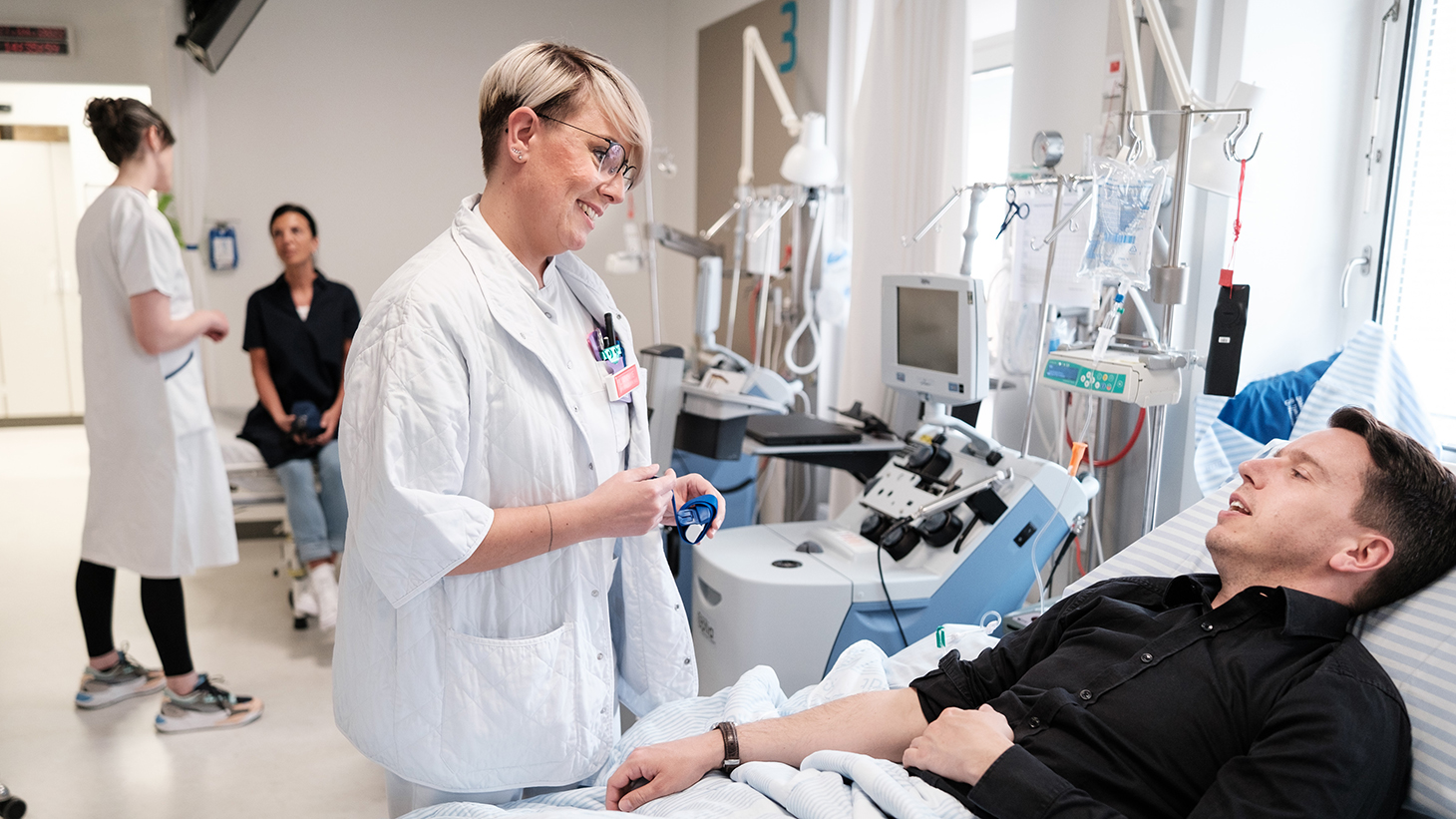 Patient ligger i hospitalsseng og får behandling samtidig med han taler med en sygeplejerske.