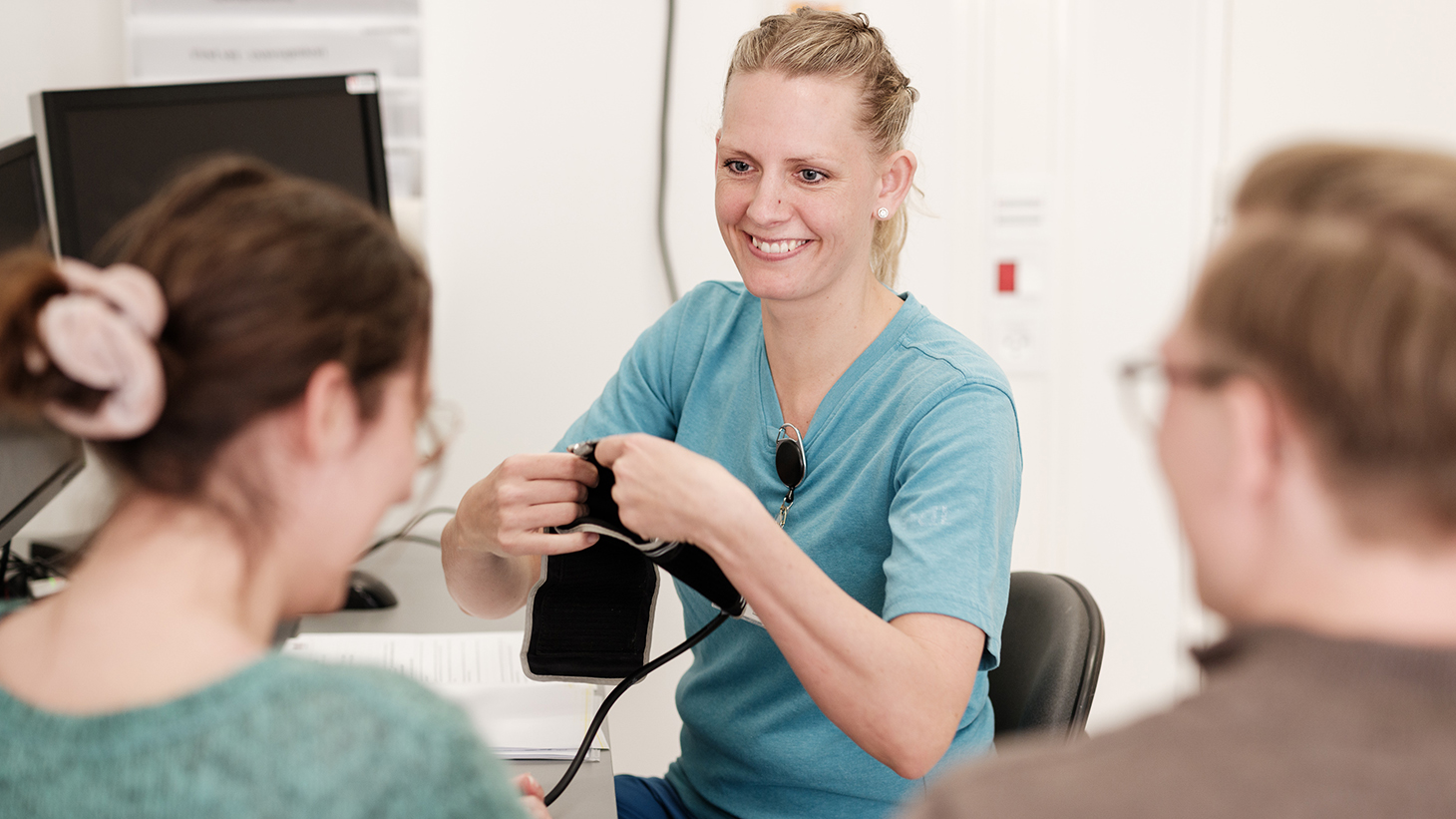 Patient og pårørende har en samtale med sundhedsfagligt personale, som skal til at tage patientens blodtryk.