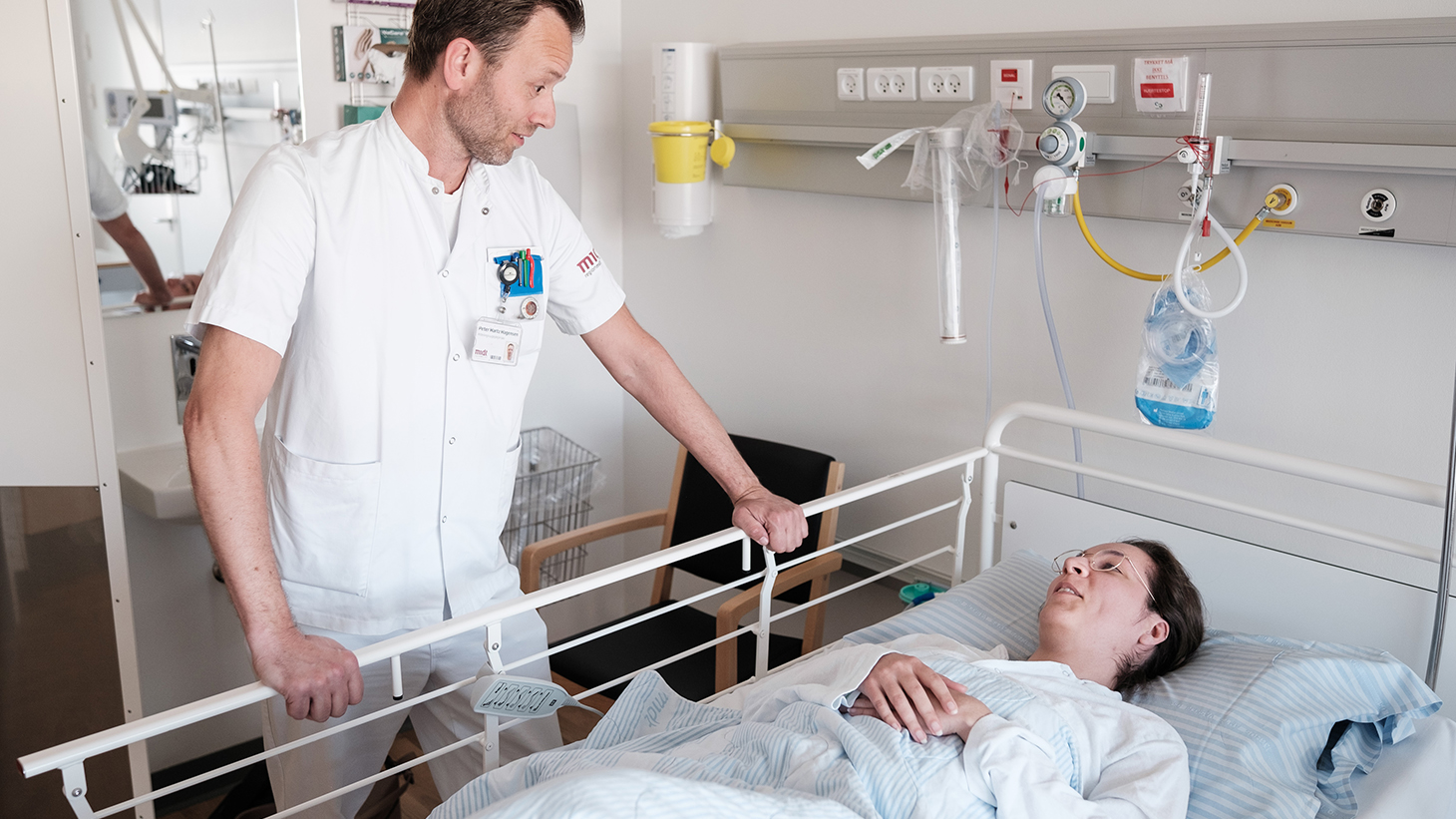 Sygeplejerske taler med patient, der ligger i en hospitalsseng
